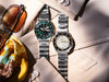 Two Seiko wristwatches with stainless steel link bracelets. One watch has a green dial and bezel, and the other has a white dial and black bezel.